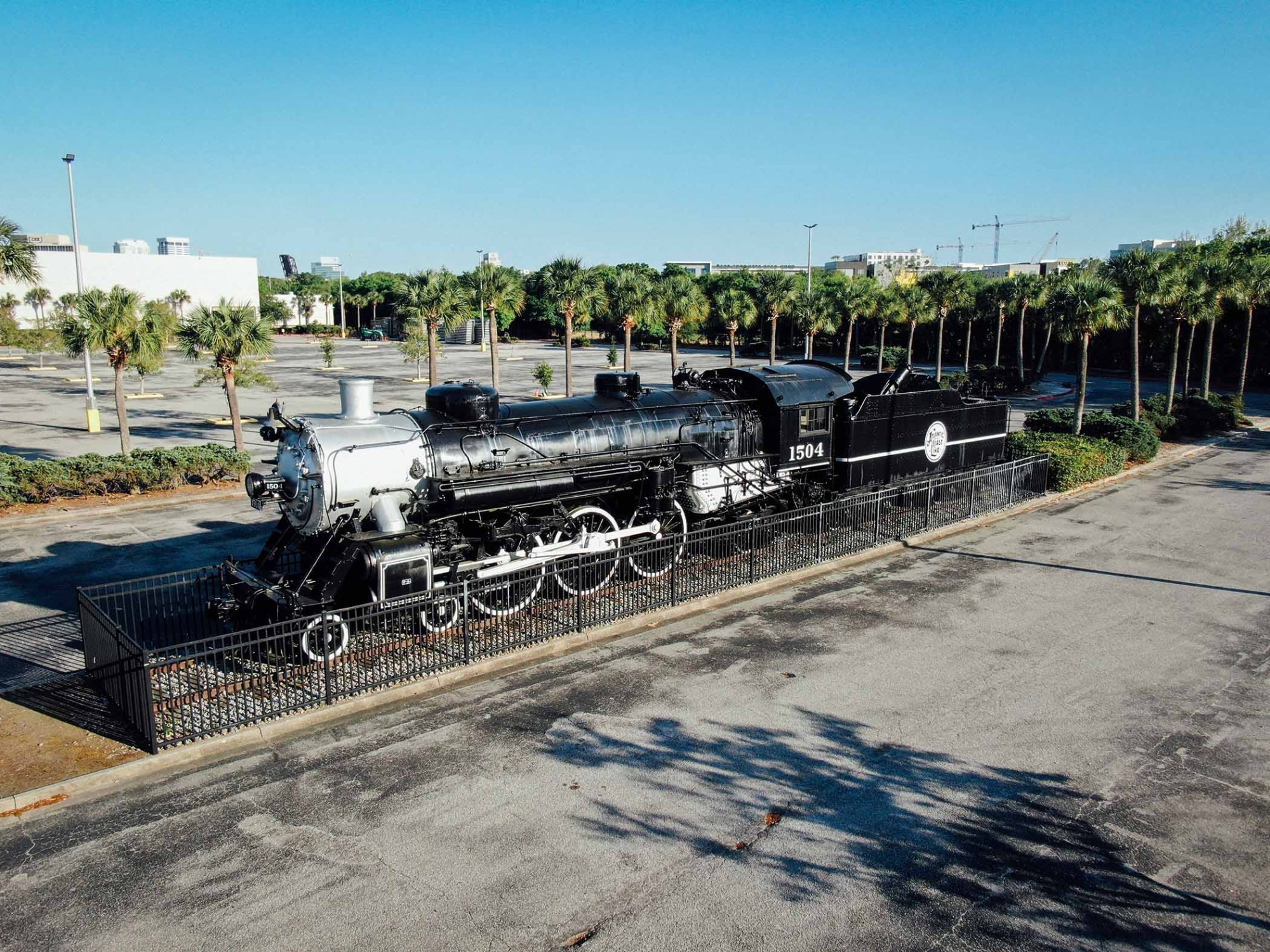 Black steam locomotive displayed outdoors behind black fencing.