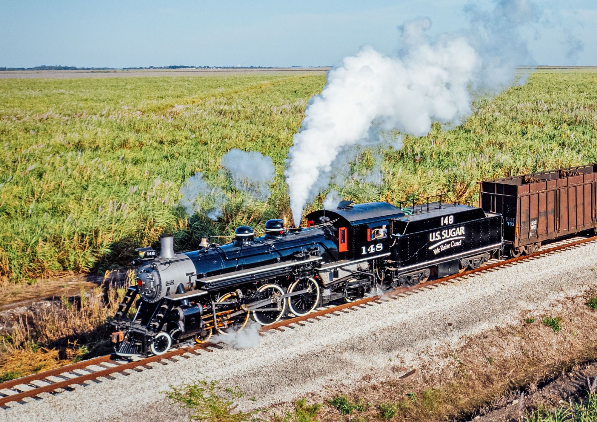 Steam locomotive traveling on tracks through a field.