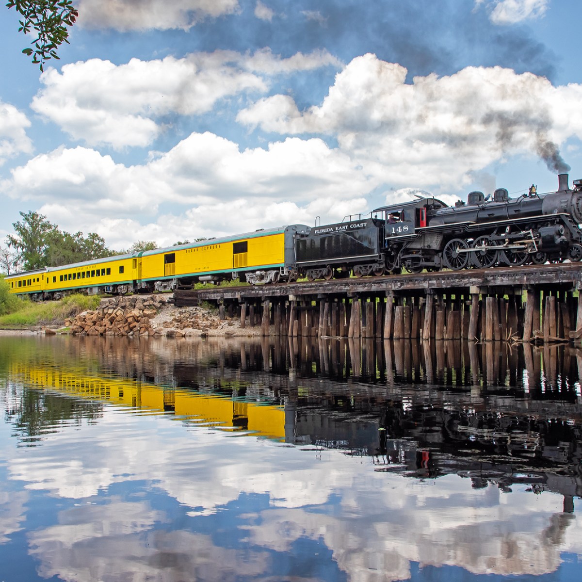 Steam train on a bridge over water with reflection.
