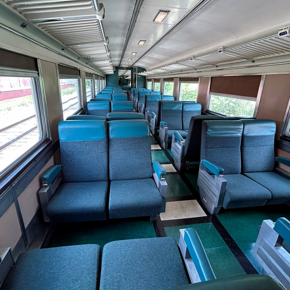 Empty train car with blue seats and large windows on both sides.