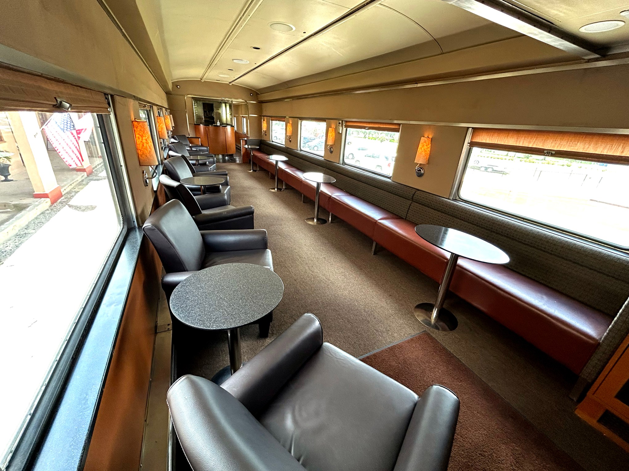 Interior of vintage train car with leather chairs and tables along windows.