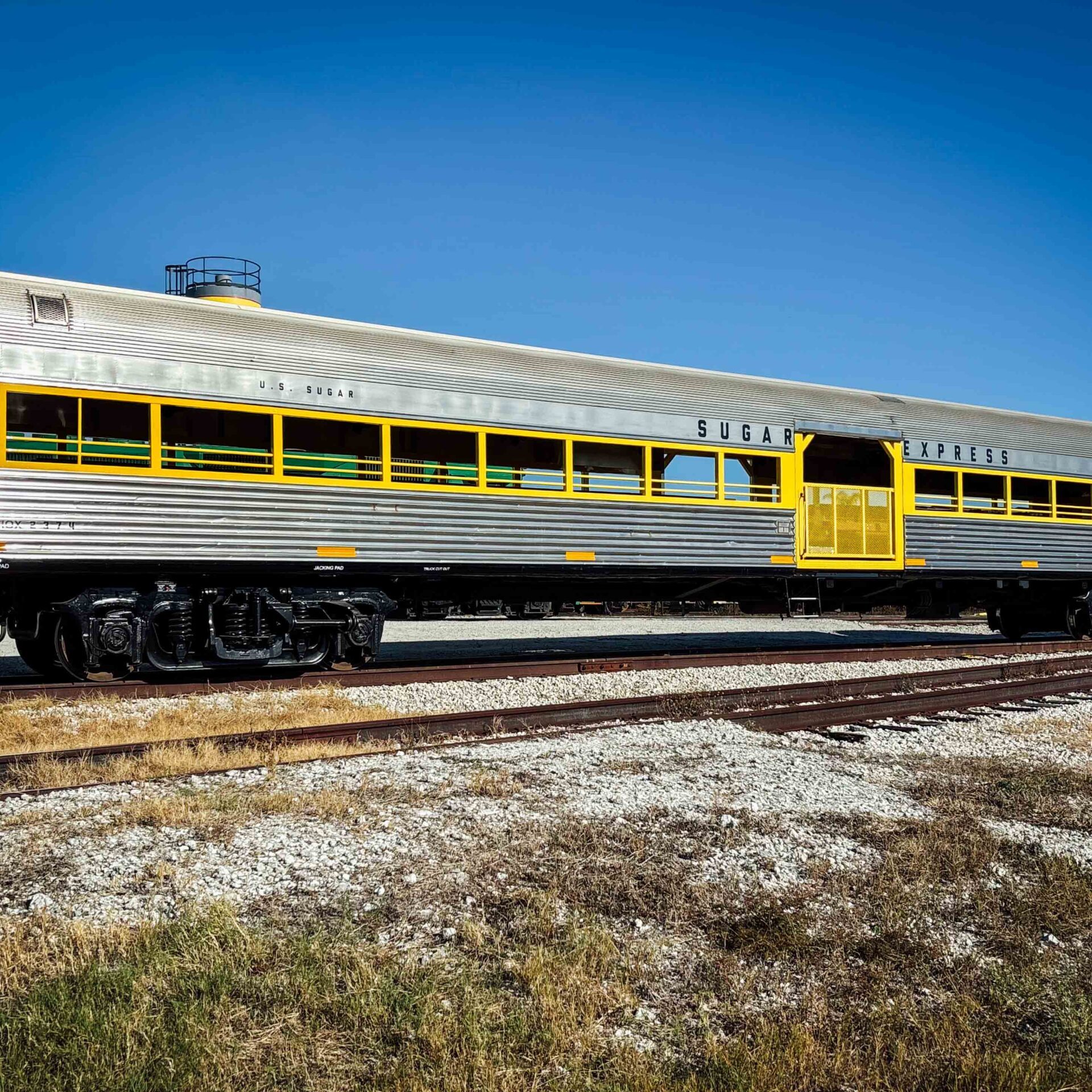 Silver and yellow train car on tracks under clear blue sky.