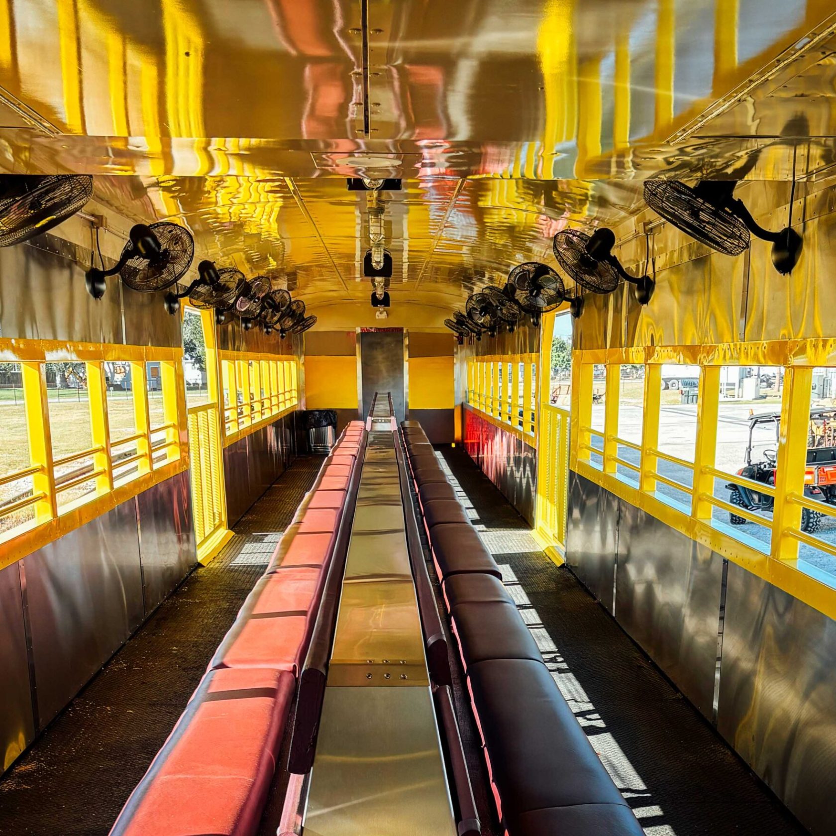 Interior view of an empty, brightly lit yellow train car with red and brown seats.