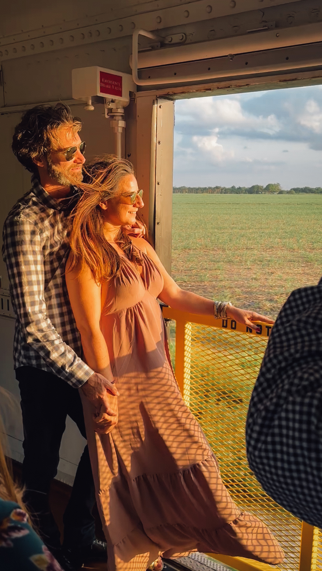 Couple enjoying scenic ride from open air Sugar Express railcar platform at sunset