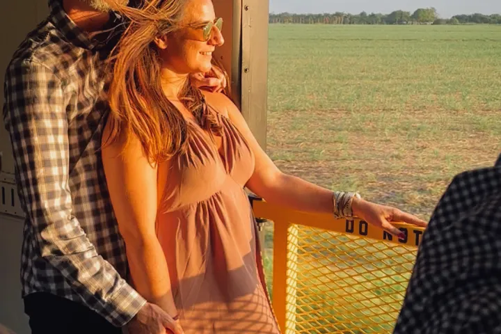 Couple enjoying sunset view from train, fields in background.