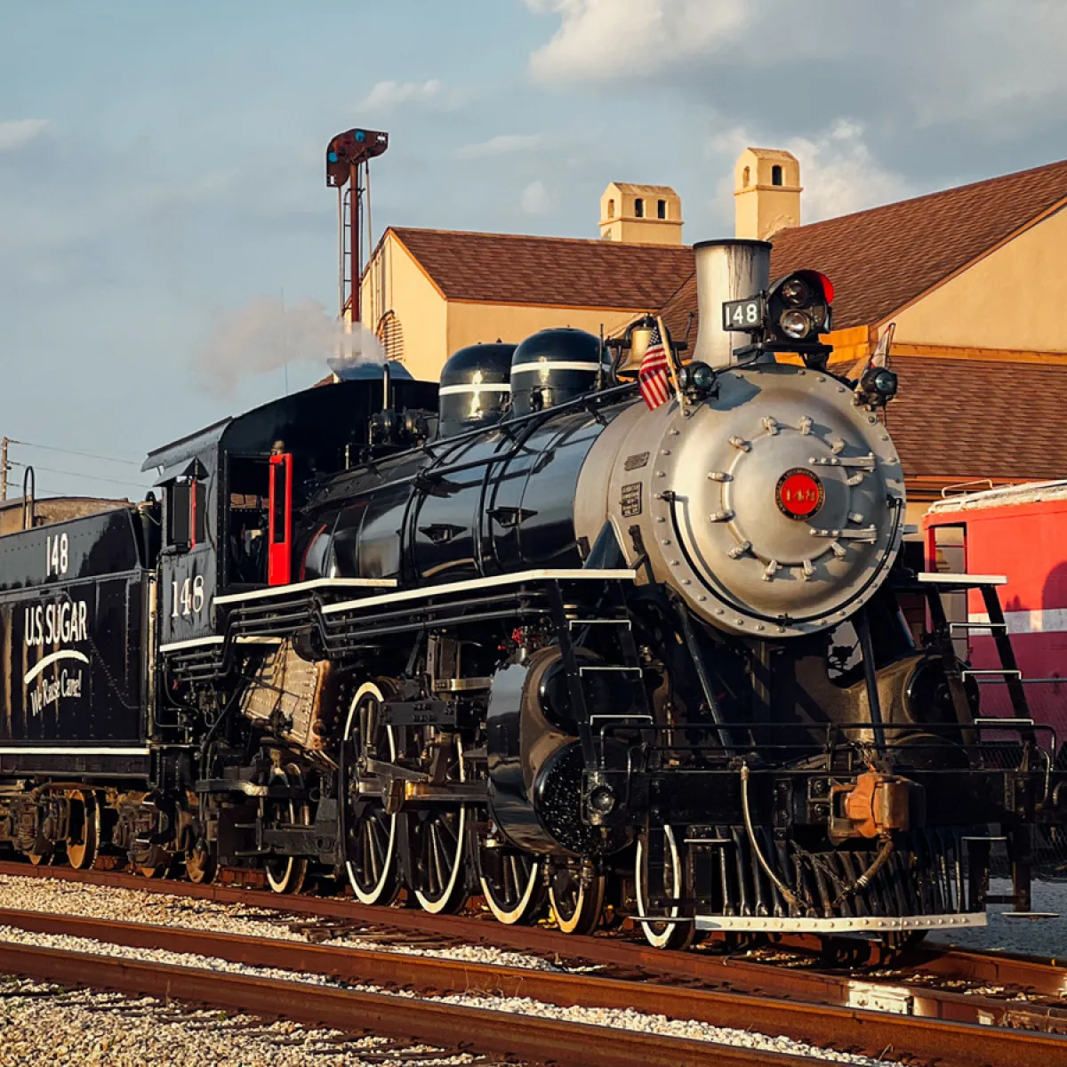 Steam locomotive with passenger cars in a train station setting.