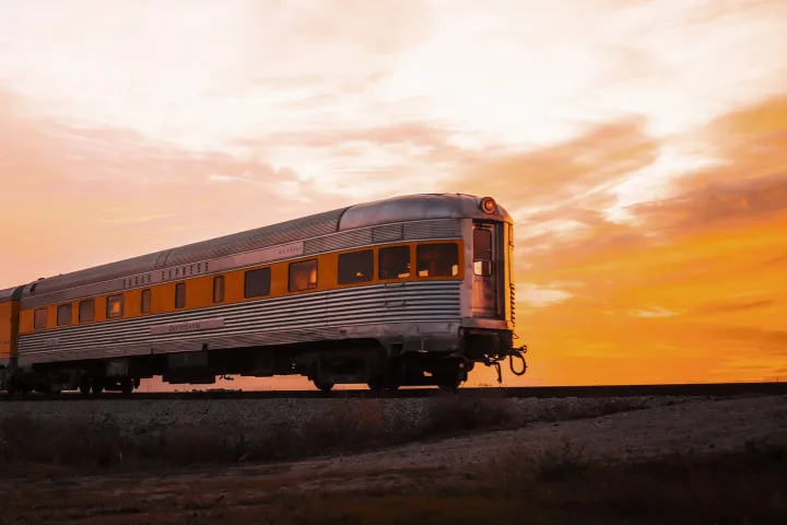 Train on tracks at sunset with orange sky.
