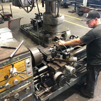 Man operating a lathe machine in a workshop setting.