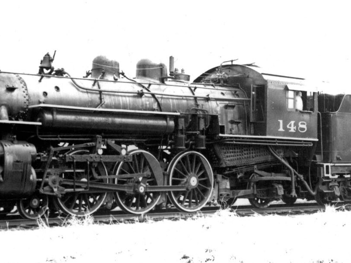Black and white image of a vintage steam locomotive on railroad tracks.