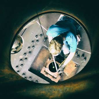 Person inside industrial equipment, viewed from above, working on metal components.