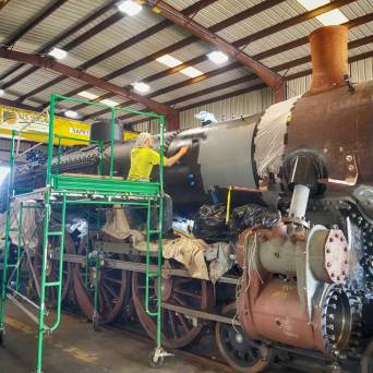 Workers restoring a large steam locomotive in a warehouse