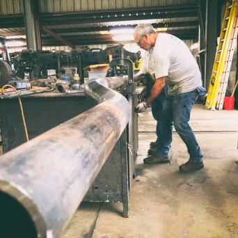 Man working on large metal pipe in industrial workshop.
