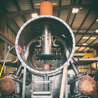 Interior view of an industrial machine with pipes, gears, and a ladder inside a warehouse.