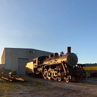 Old steam locomotive near a warehouse during sunset.