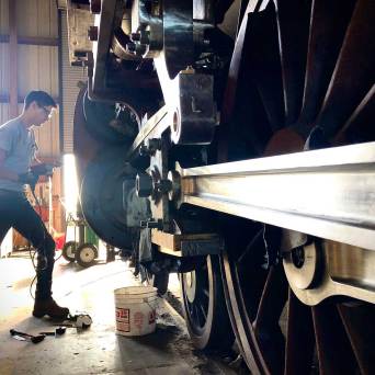 Person inspecting large train wheels inside a workshop.