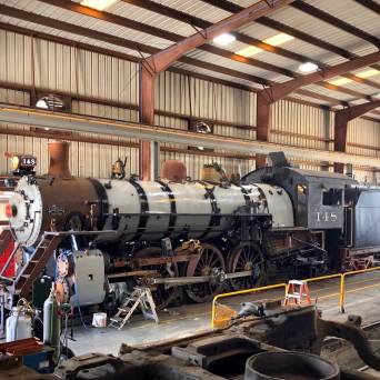 Steam locomotive in a maintenance shed with tools and equipment around.