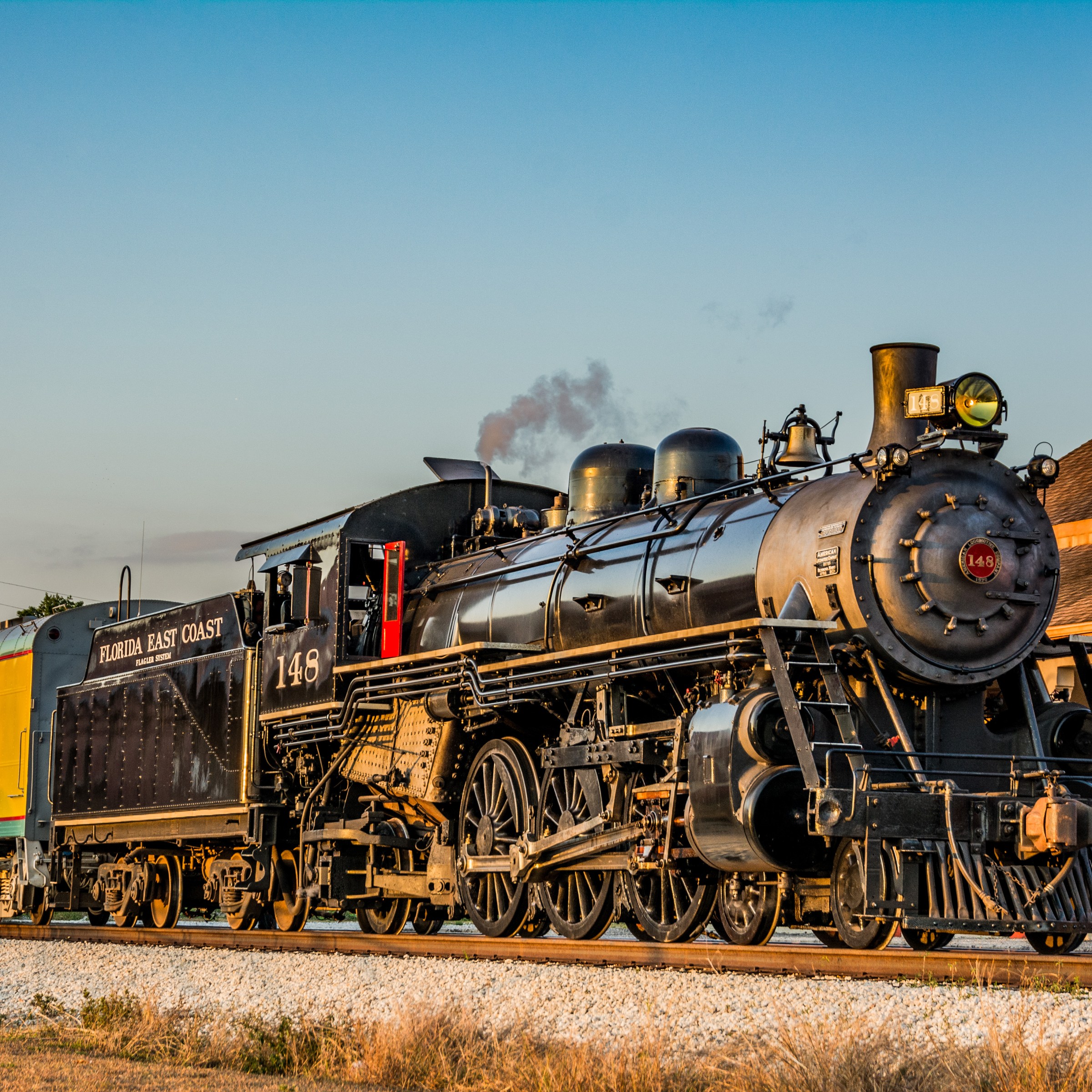 Vintage steam locomotive with freight cars on tracks near a station.
