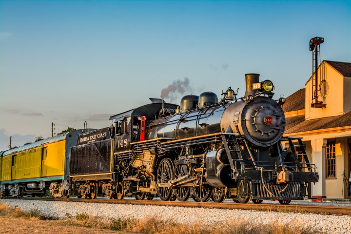 Vintage steam locomotive with freight cars on tracks near a station.