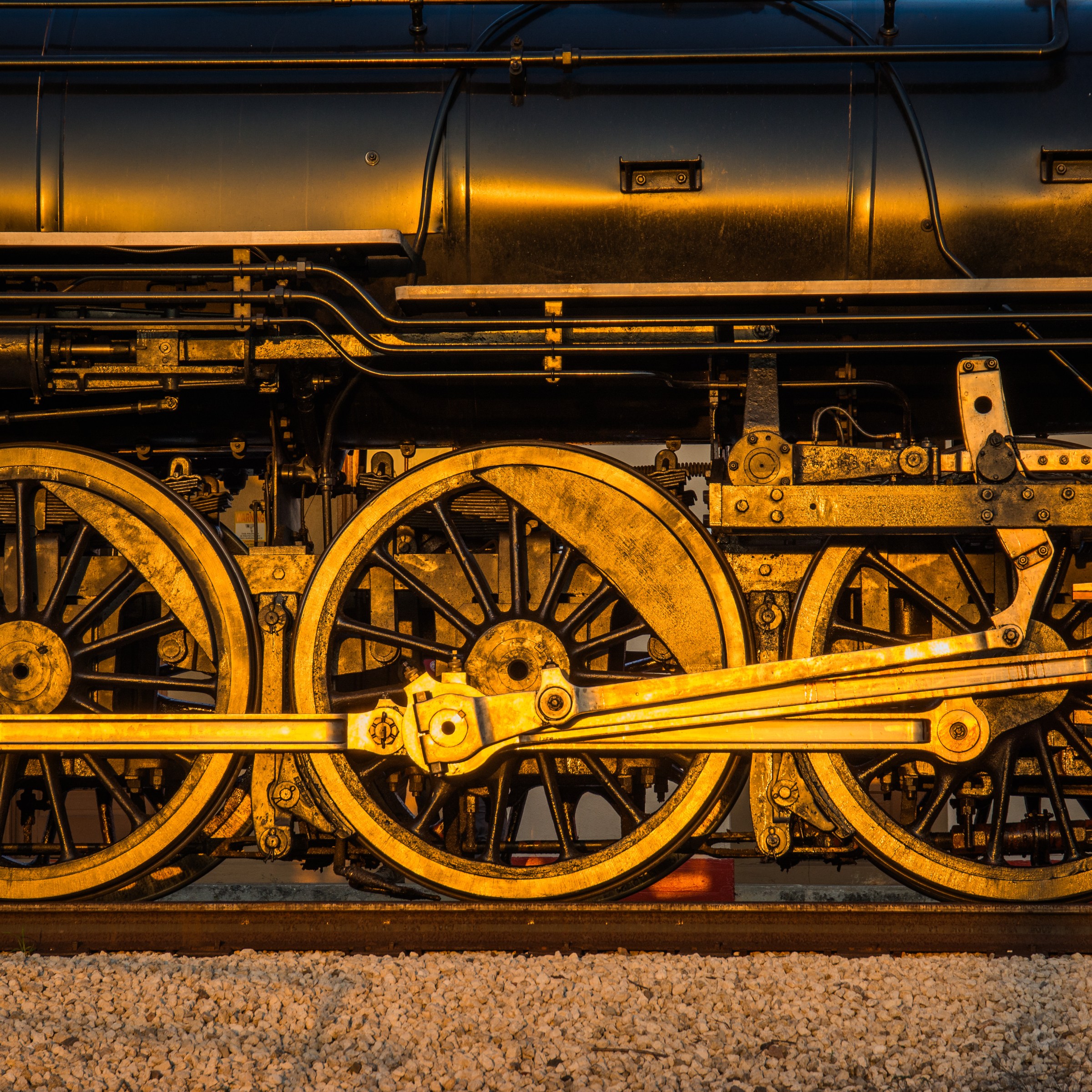Close-up of train wheels and machinery, illuminated by warm light.