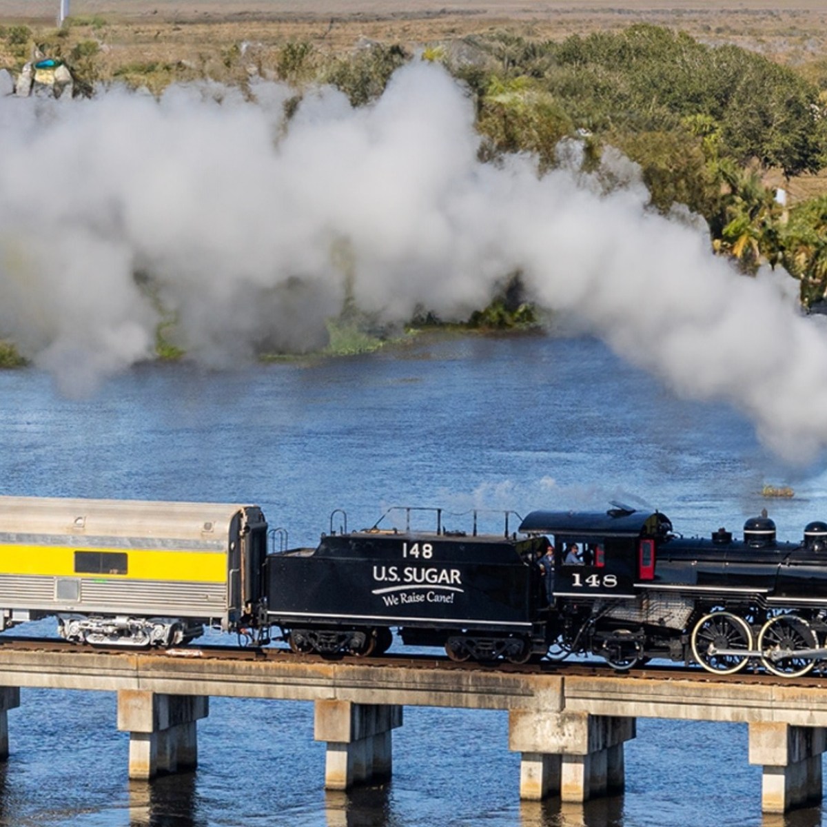 Steam locomotive crossing a bridge over water, emitting smoke.