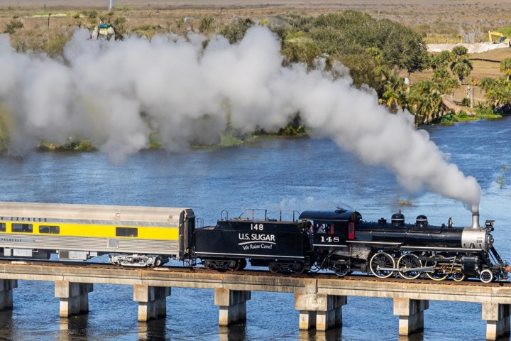 Steam locomotive crossing a bridge over water, emitting smoke.