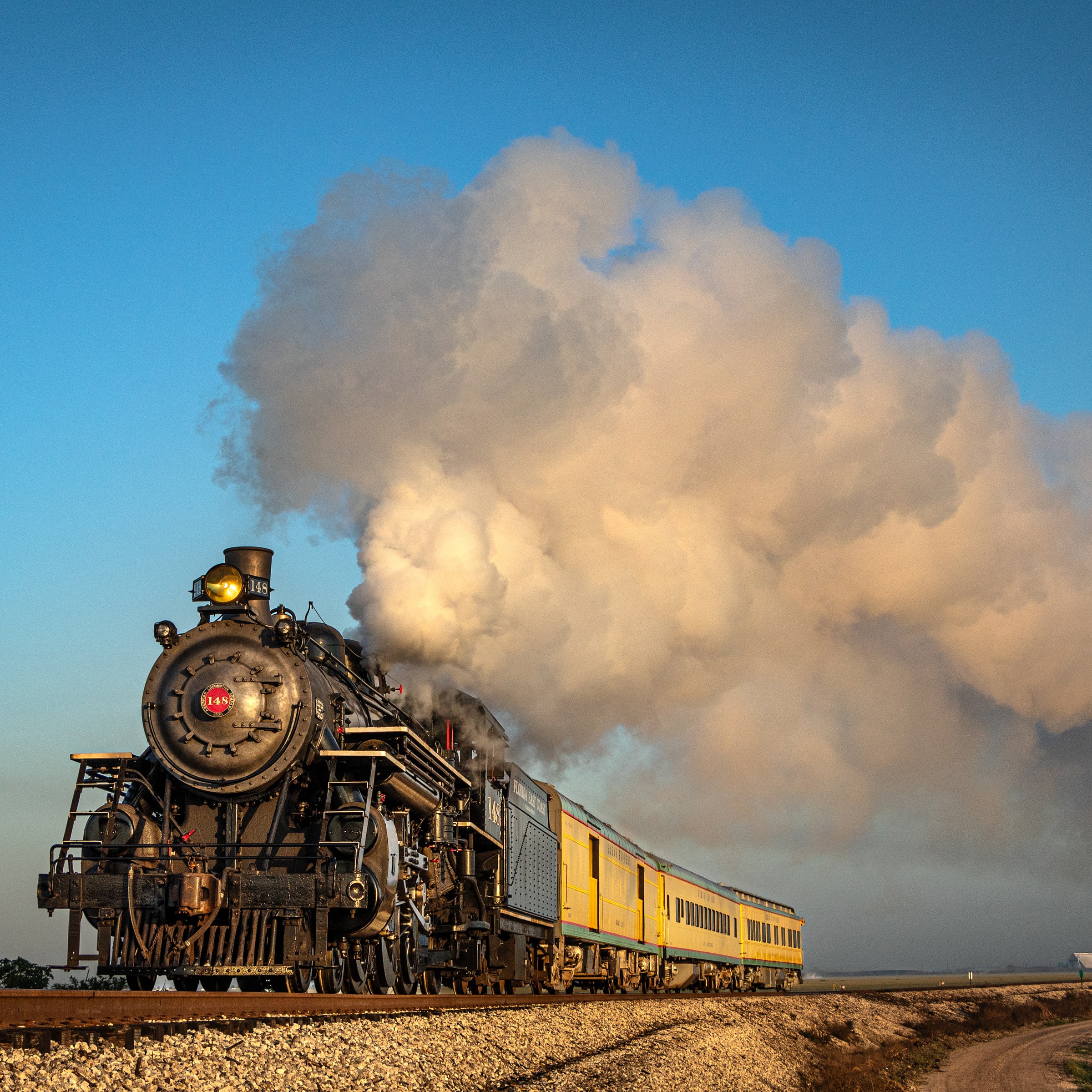 Vintage steam locomotive on tracks with billowing smoke under a clear sky.