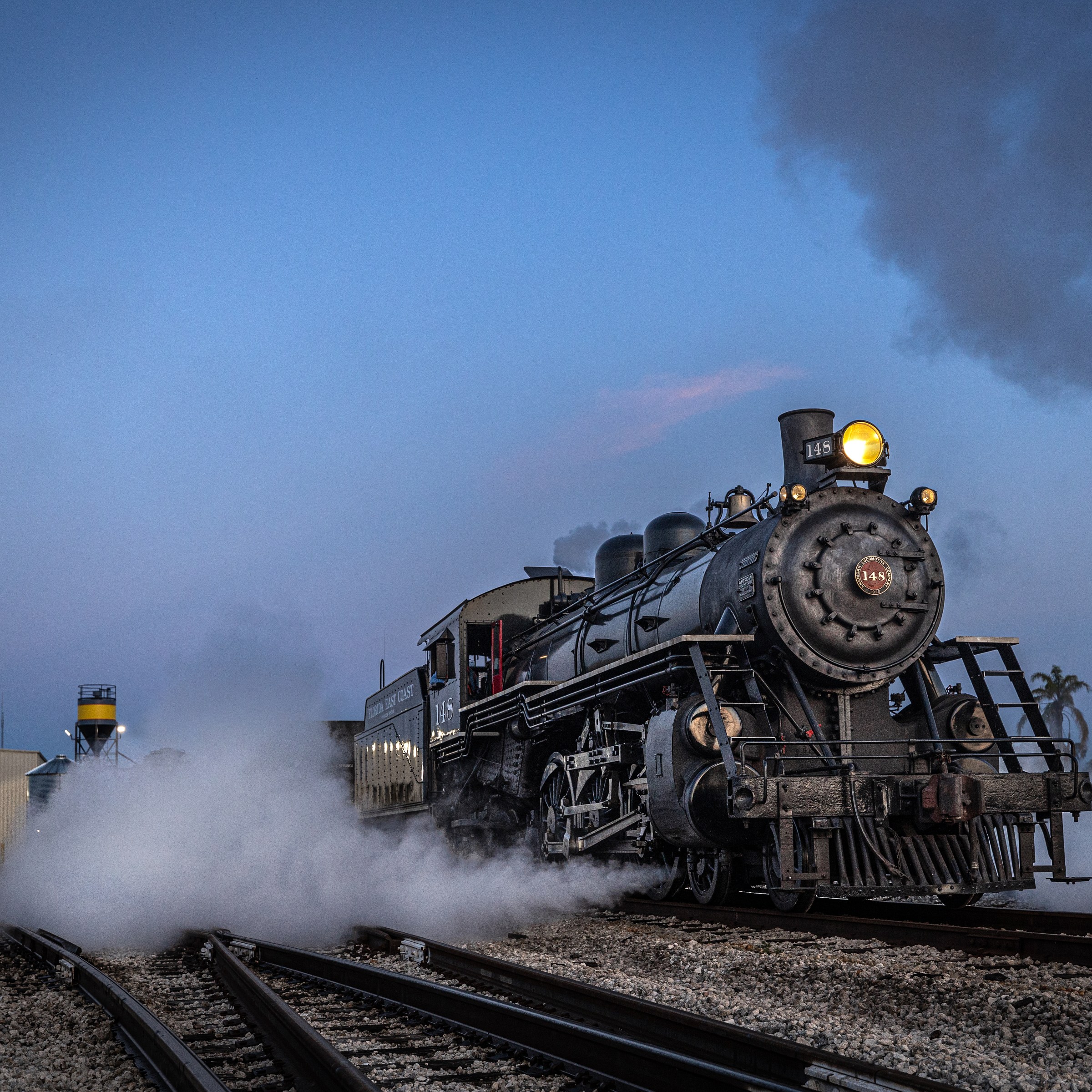 Steam locomotive on tracks with smoke in the evening.