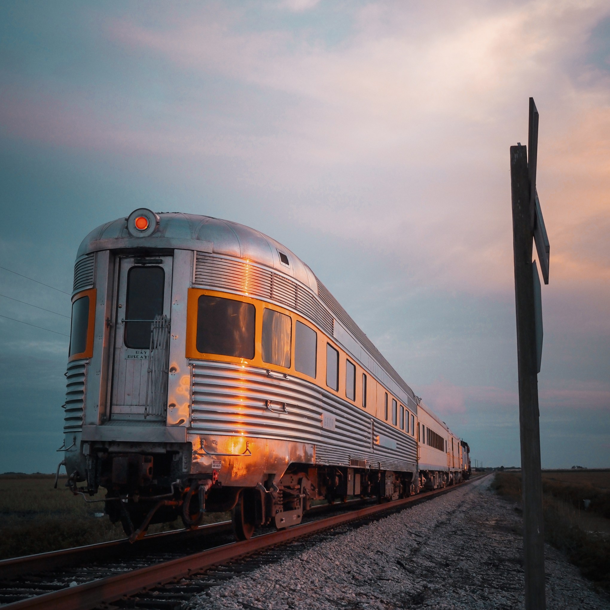 Retro train on tracks during sunset with cloudy sky.