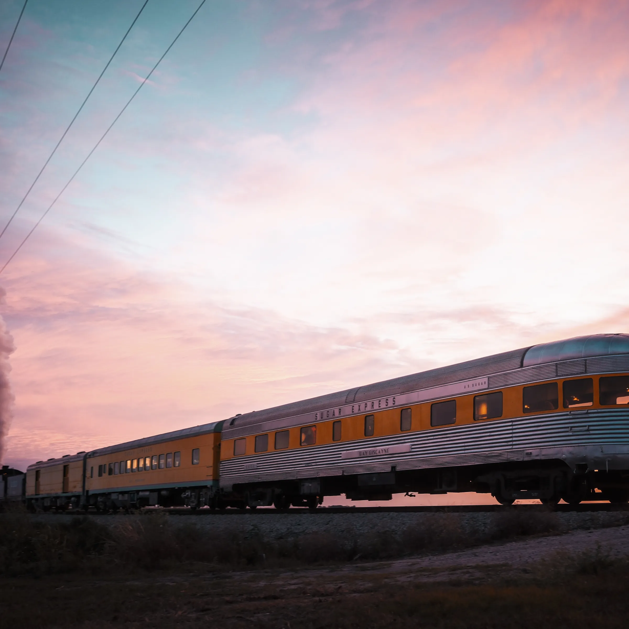 Steam train with orange cars at sunset on open track.