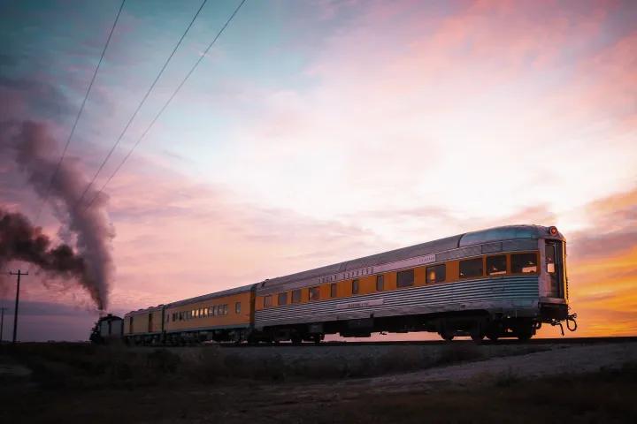 Steam train with orange cars at sunset on open track.