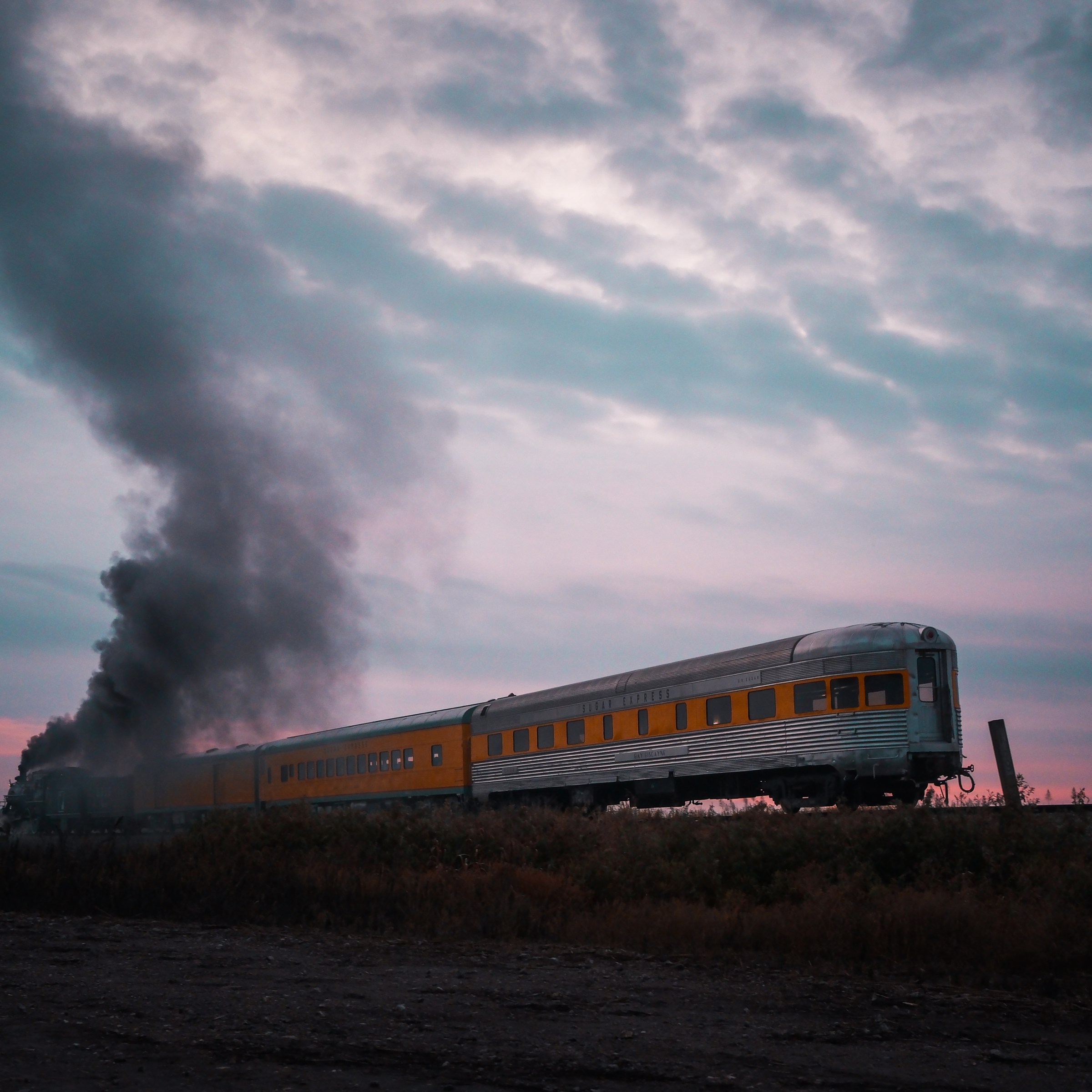 Train emitting dark smoke under a cloudy sky during sunset.