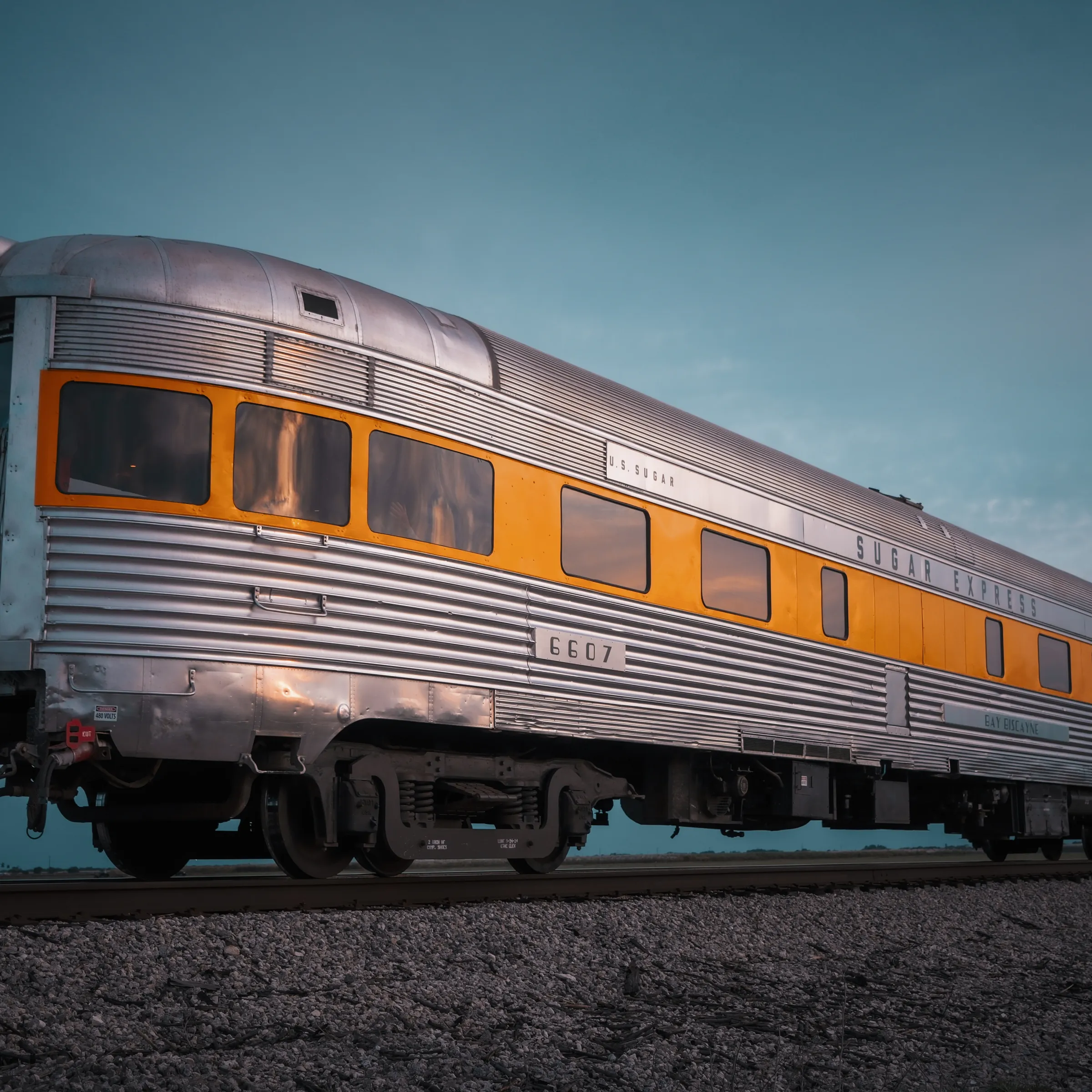 Vintage silver train car with yellow stripe on tracks at sunset.