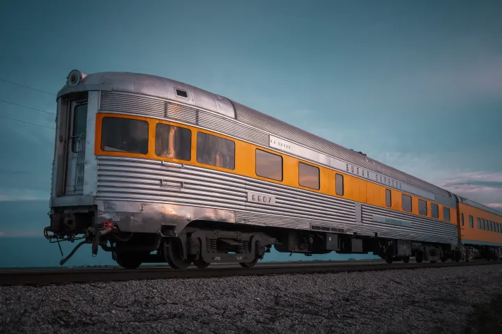Vintage silver train car with yellow stripe on tracks at sunset.
