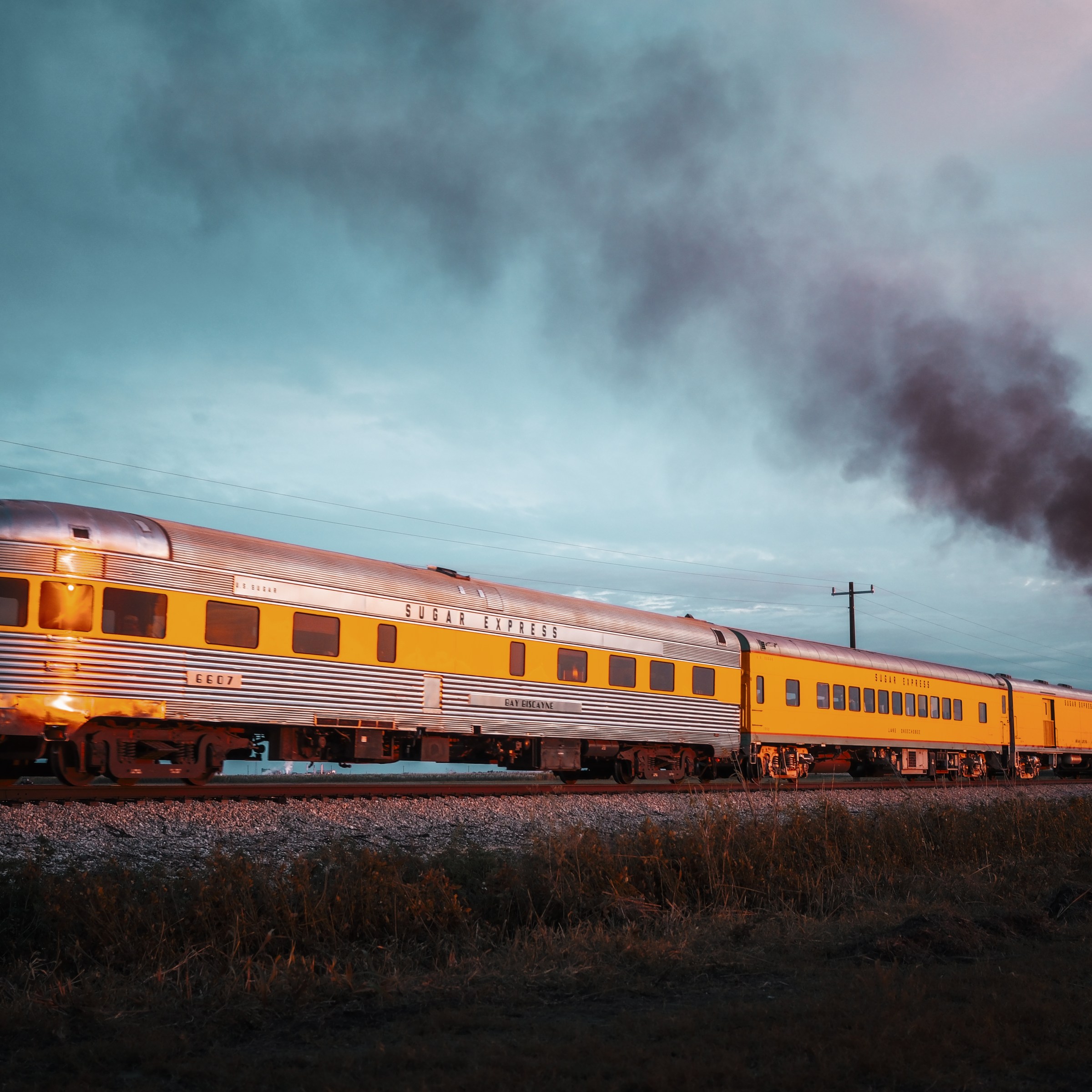 Vintage yellow train emitting smoke under a cloudy sky.
