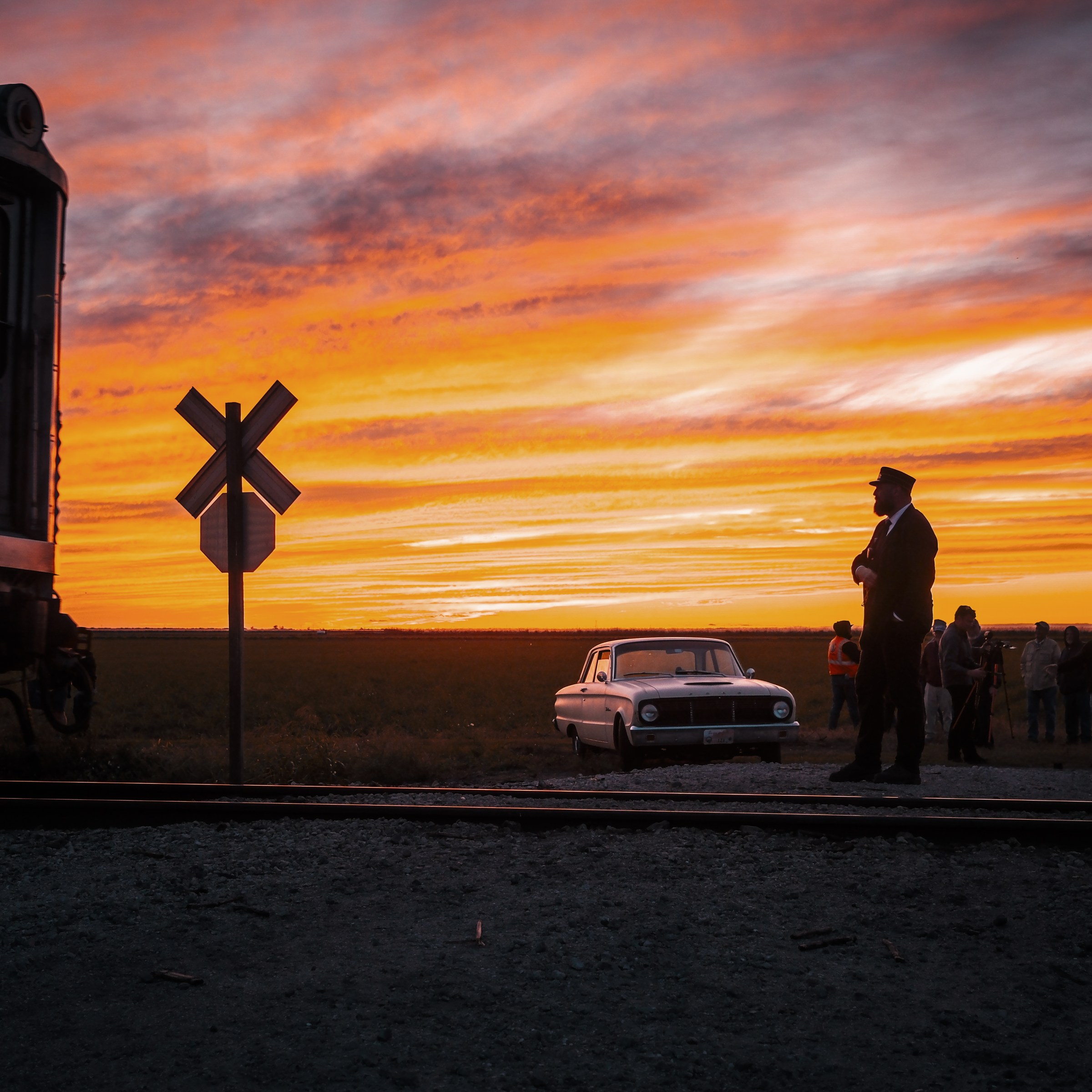 Train at sunset with people and car near crossing