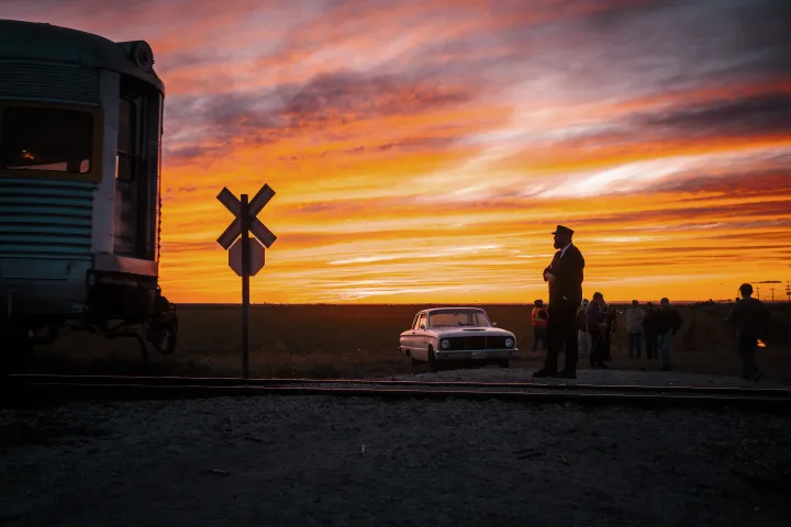 Train at sunset with people and car near crossing