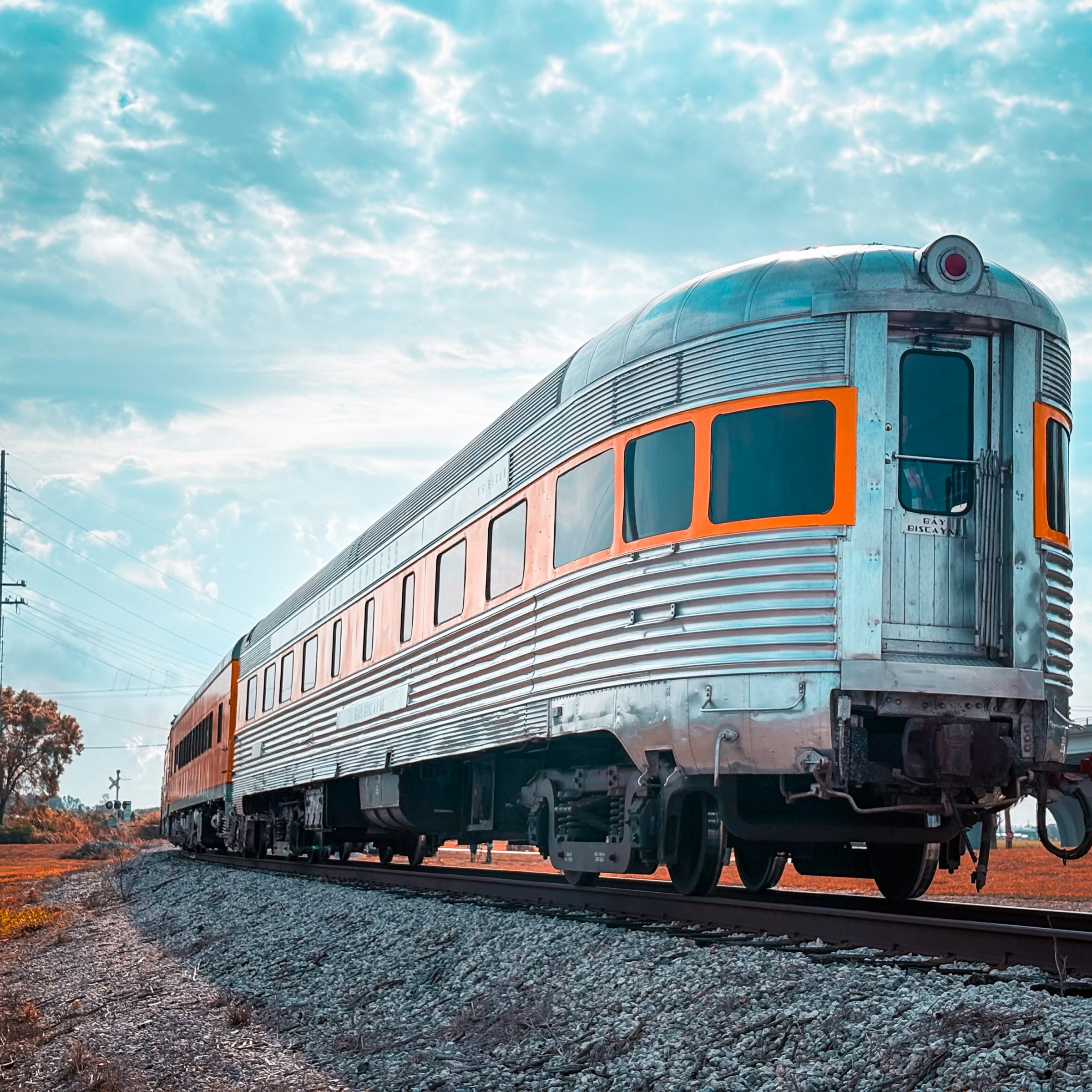 Vintage silver train on tracks under a partly cloudy sky.