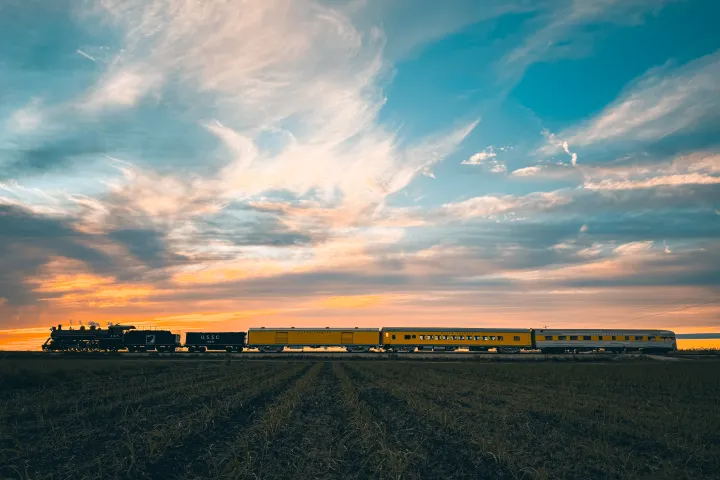 Steam train with yellow carriages under a colorful sunset sky.