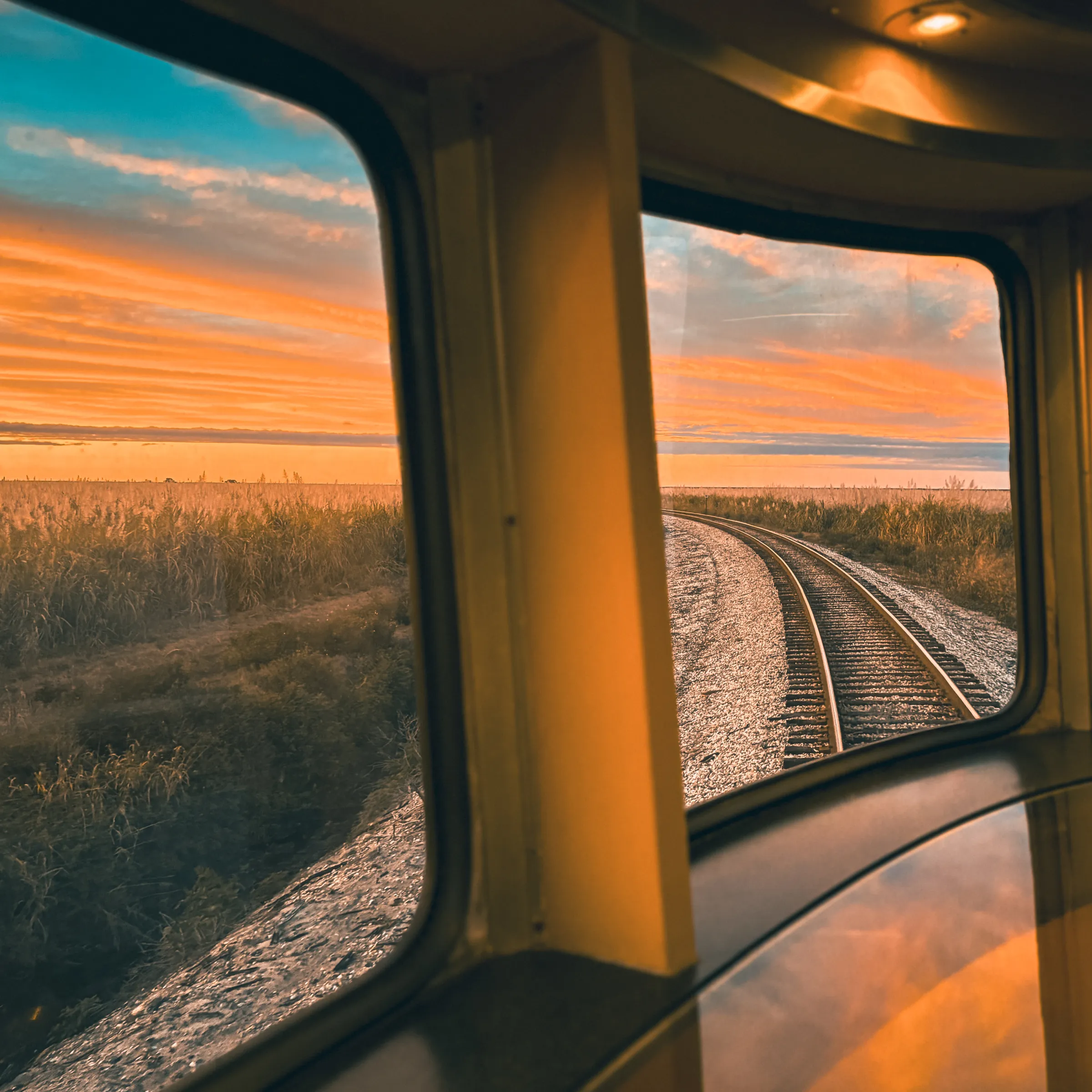 View from train window showing tracks and colorful sunset sky.