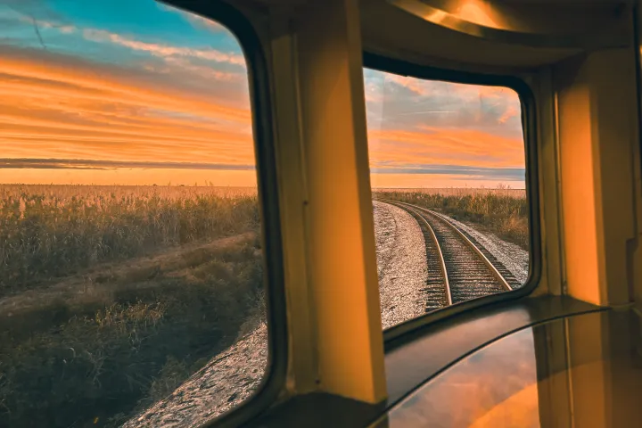 View from train window showing tracks and colorful sunset sky.