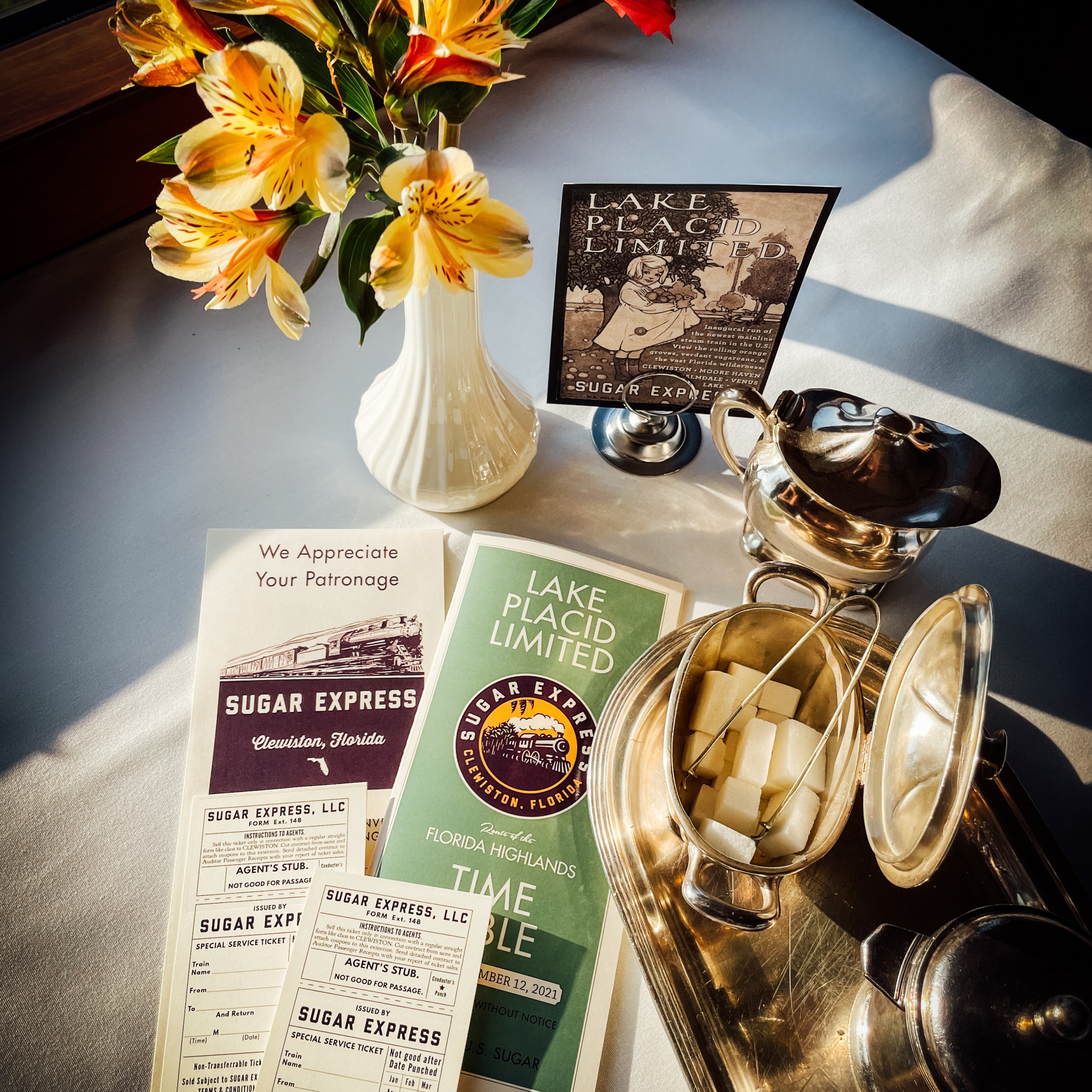 Vintage train tickets and brochures on a table with flowers and a sugar bowl.
