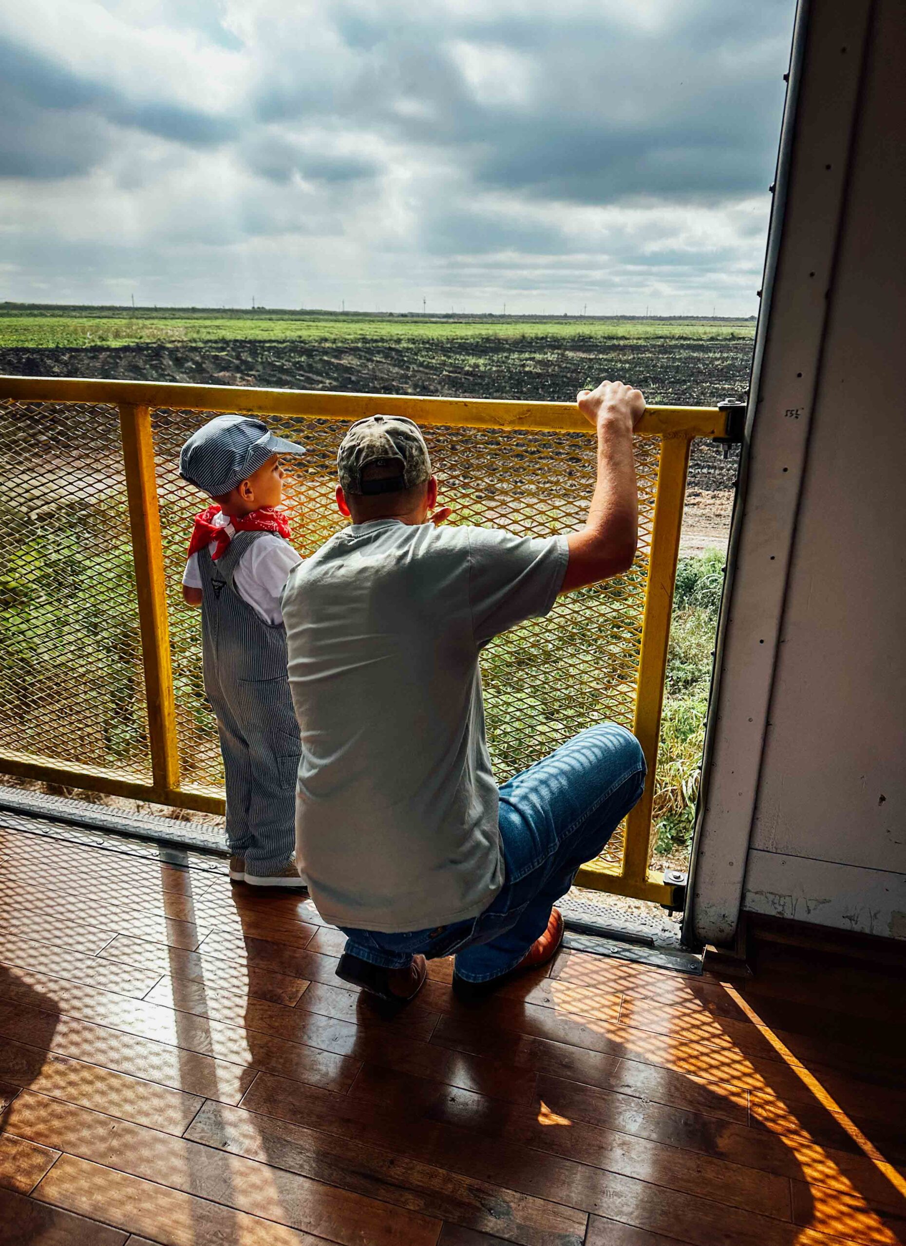 Adult and child standing on open air Sugar Express railcar platform overlooking Florida agricultural fields