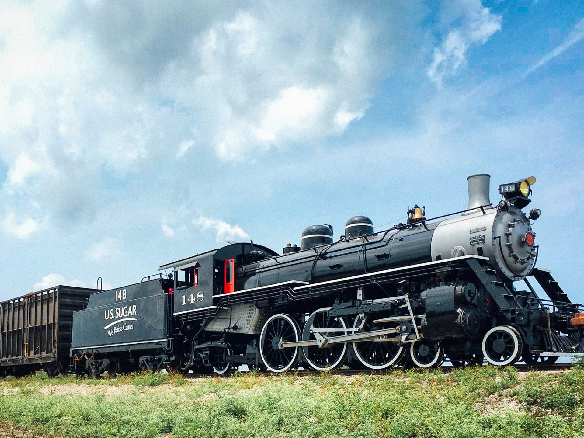 Steam locomotive on tracks under a partly cloudy sky.