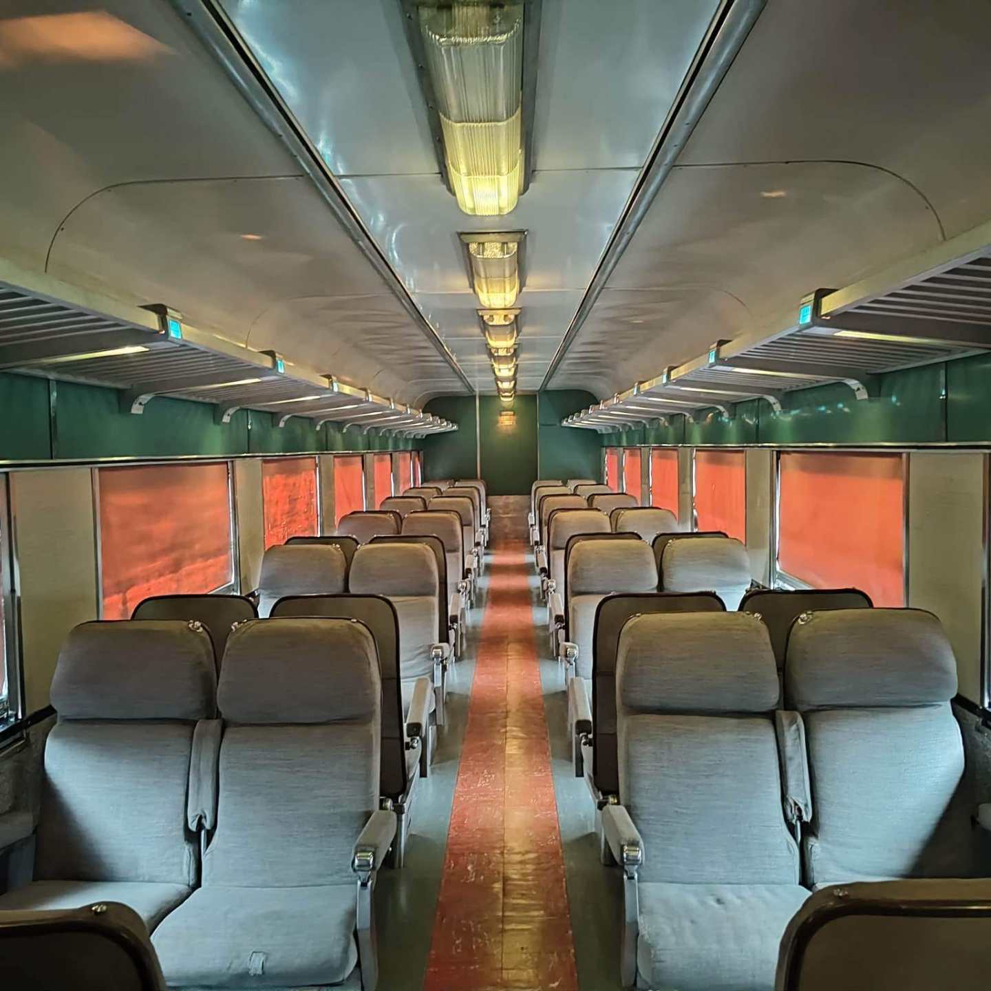 Empty train car interior with rows of beige seats and red curtains.