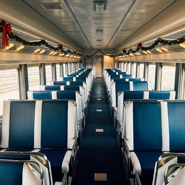 Empty train car with blue seats and holiday garlands on the ceiling.