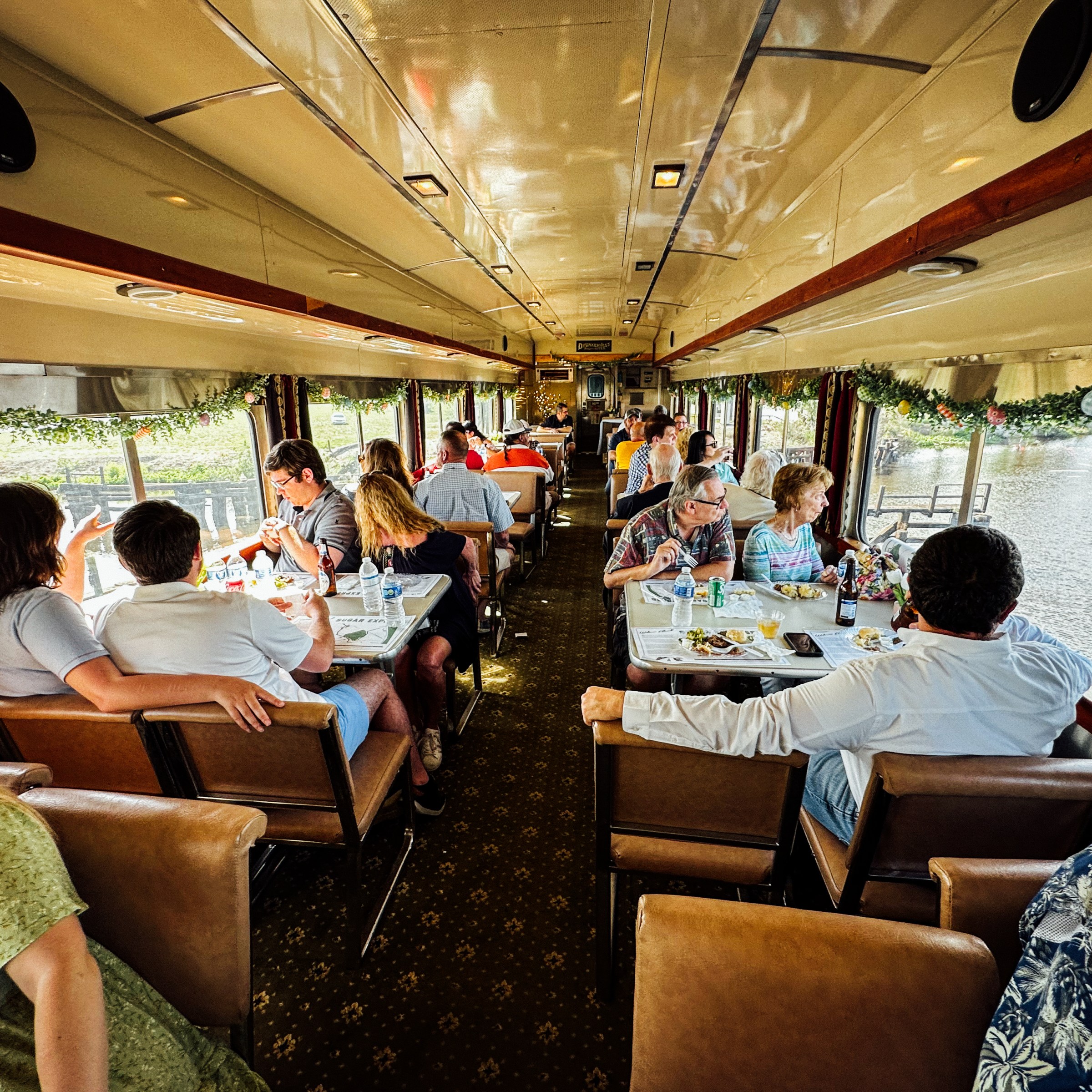 People dining in a vintage train car with windows, daytime.