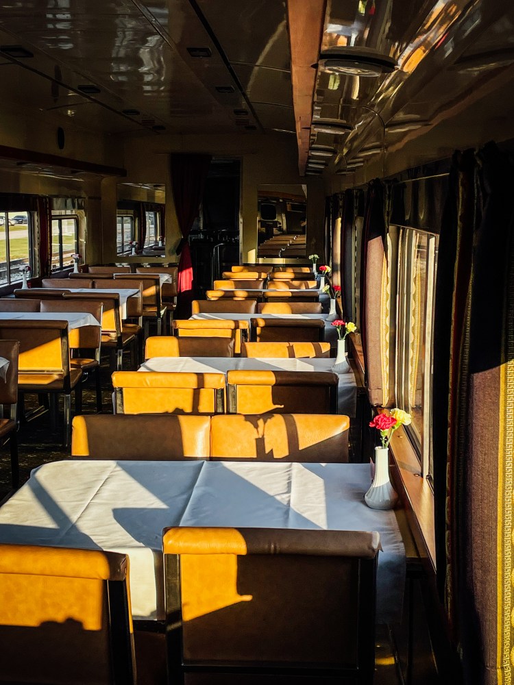 Sunny train dining car with set tables and vases with flowers.