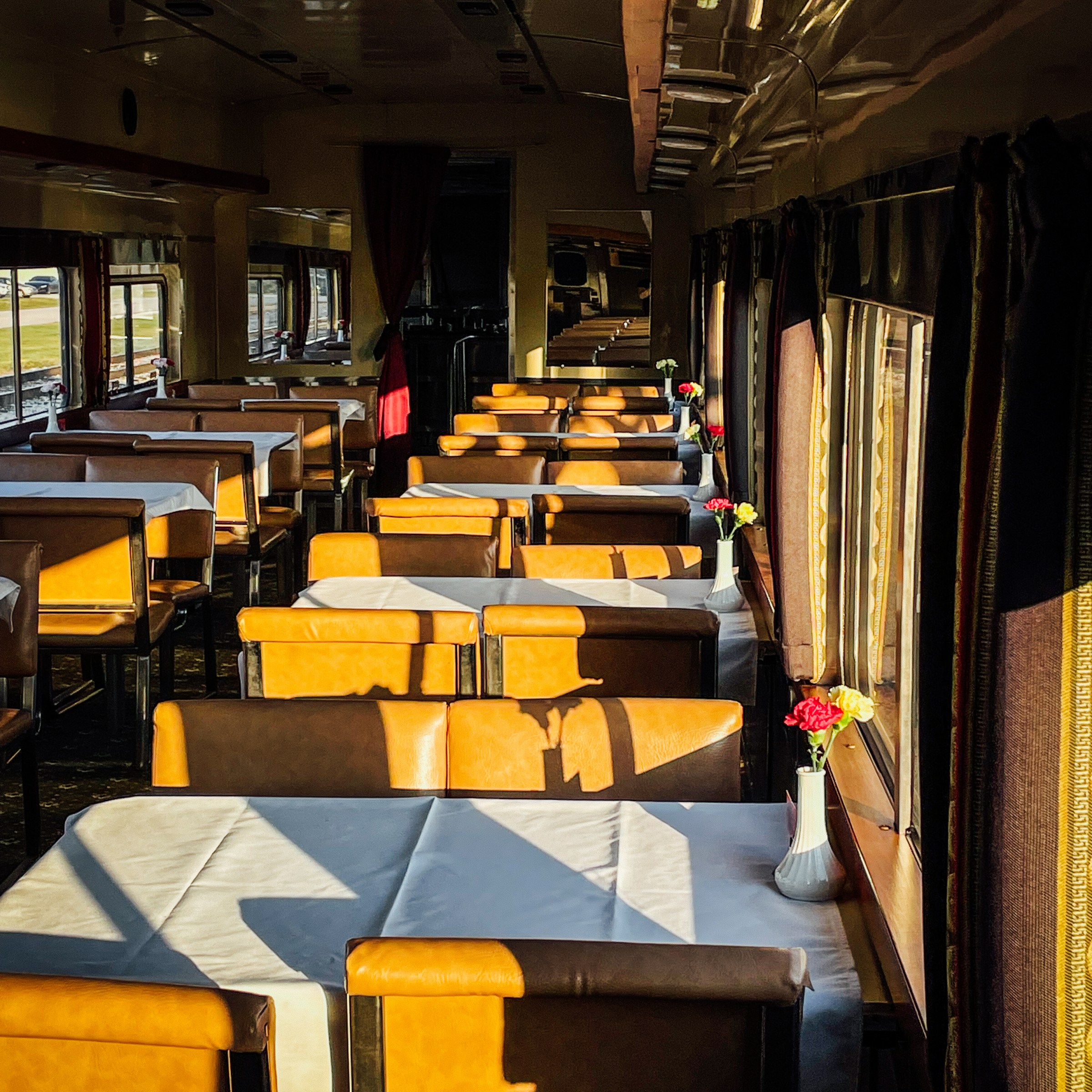 Sunny train dining car with set tables and vases with flowers.