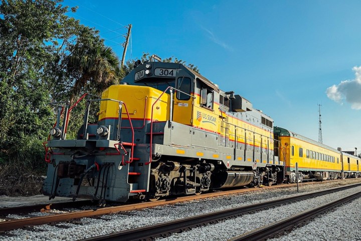 Yellow and gray train on railroad tracks under blue sky.