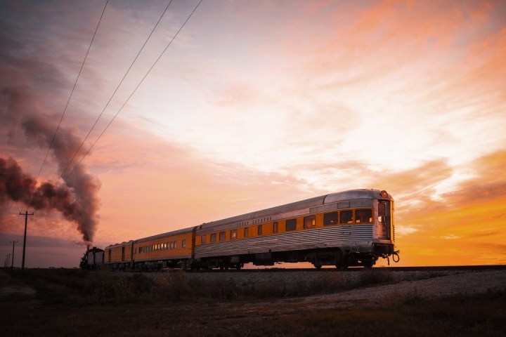 Train traveling on tracks at sunrise with smoke trailing behind